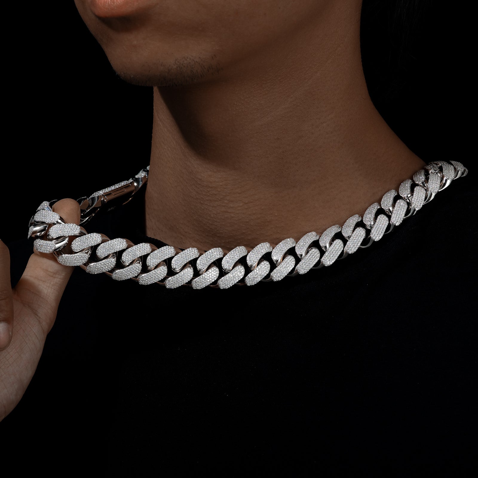 Silver chain necklace being held by a hand against a dark background