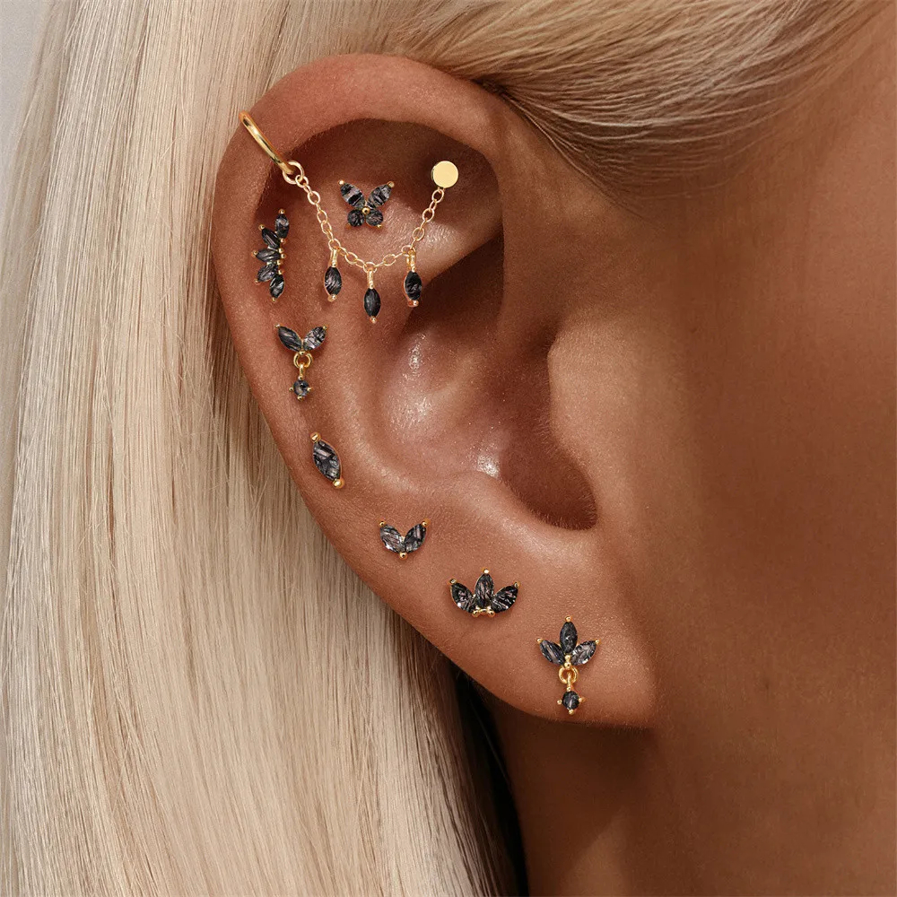 Close-up of an ear with multiple gold and black earrings.