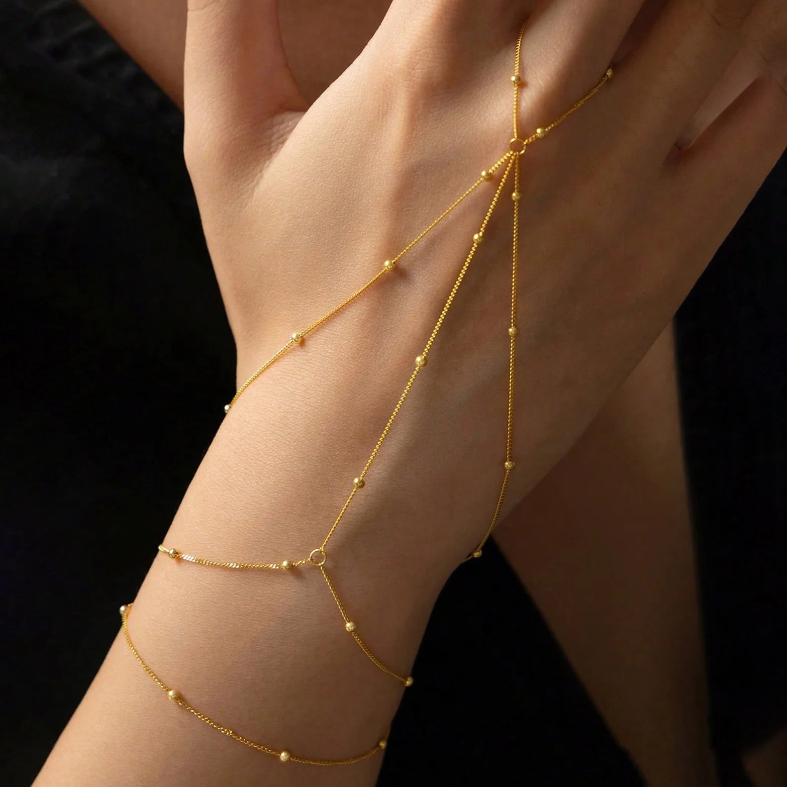 Gold arm chain on a person's arm against a dark background