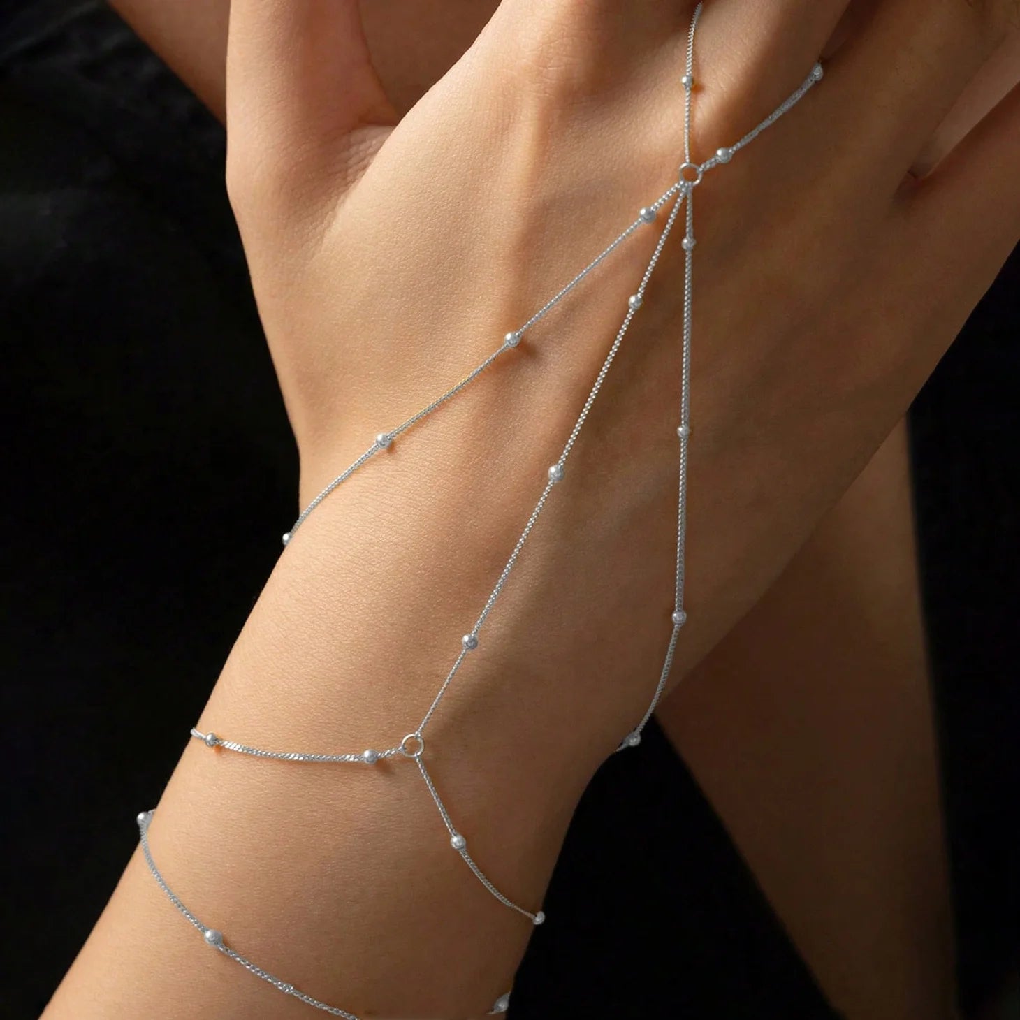Silver body chain on a person's arm against a black background