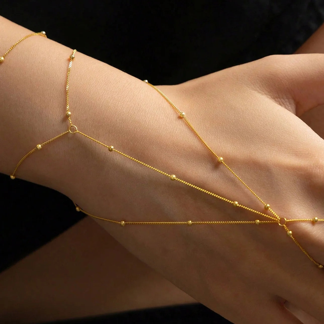 Gold bracelet on a wrist against a black background