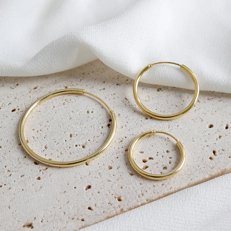 Three gold hoop earrings on a textured surface with a white fabric background