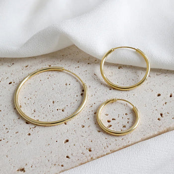 Three gold hoop earrings on a textured surface with a white fabric background