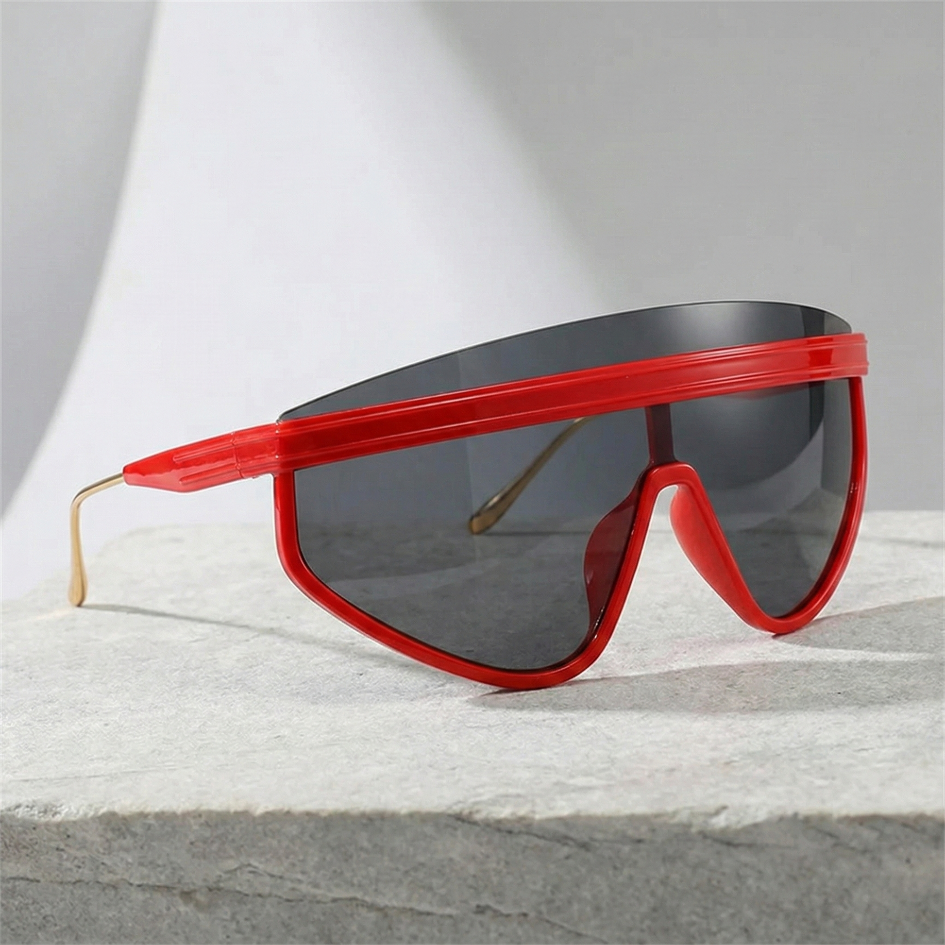 Sunglasses with red frame and black lenses on a light gray surface
