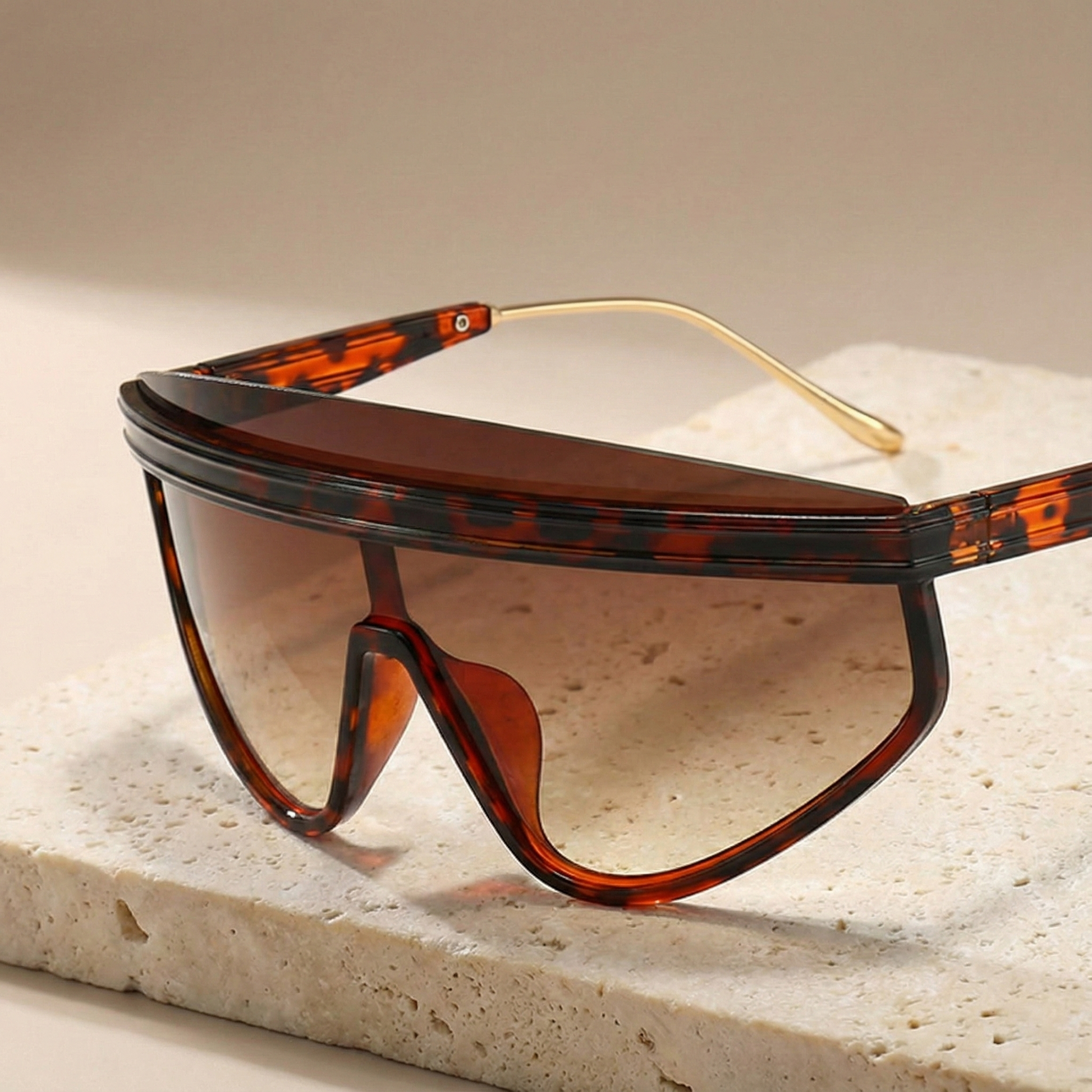 Sunglasses with a tortoiseshell frame and clear lenses on a stone surface.