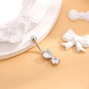 Silver belly button ring with clear gemstones on a beige surface with white bows.