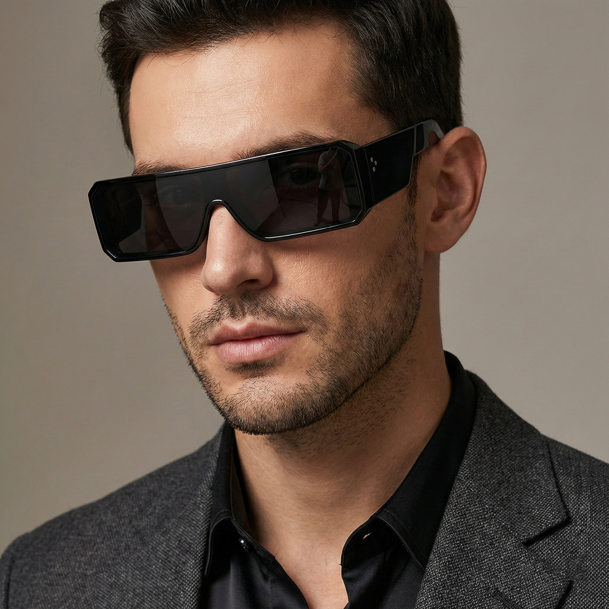 Man wearing black sunglasses and a gray blazer against a neutral background