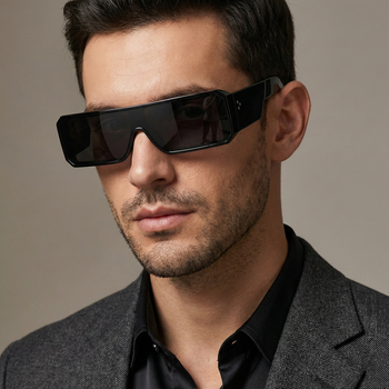 Man wearing black sunglasses and a gray blazer against a neutral background
