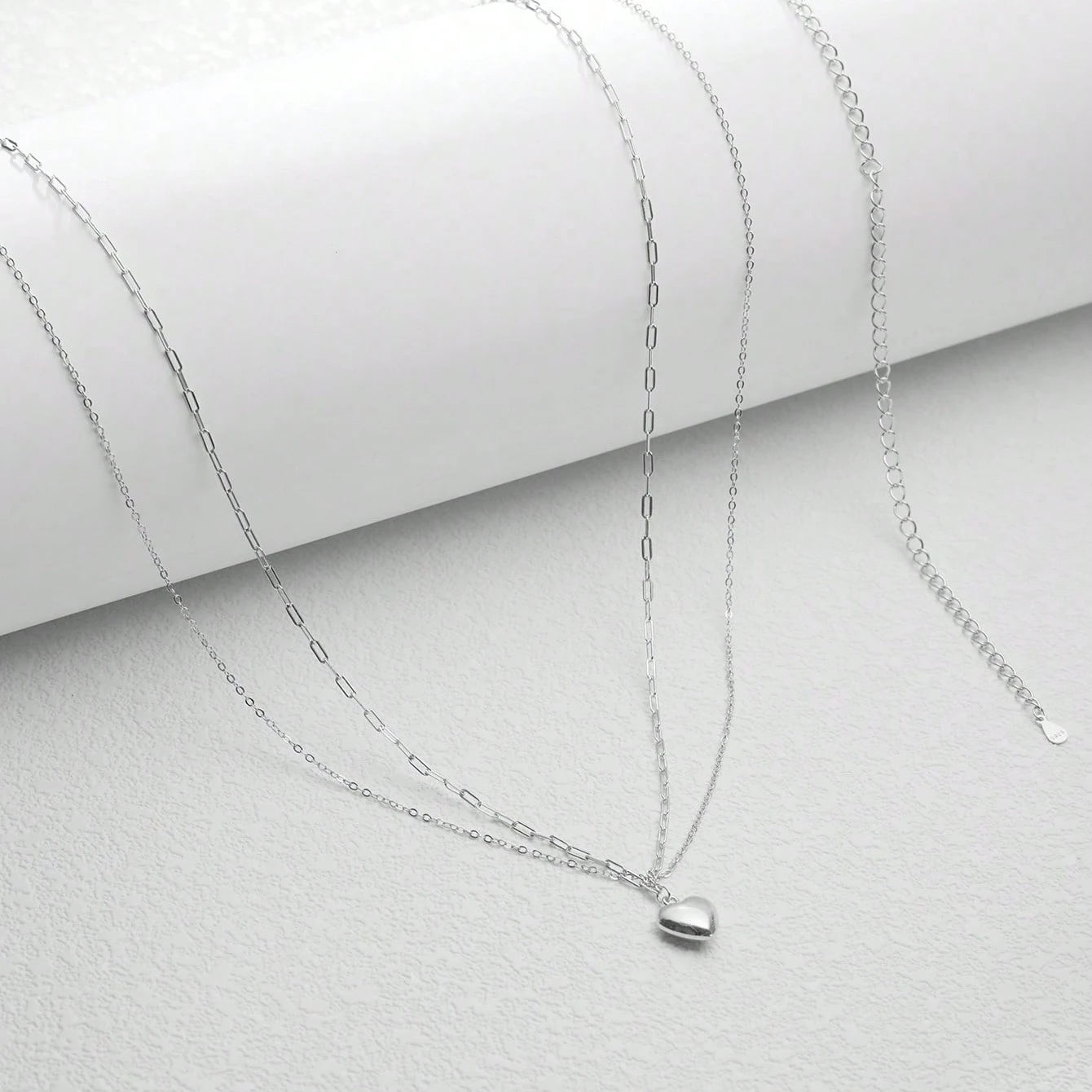 Silver necklace with a heart pendant on a light gray background