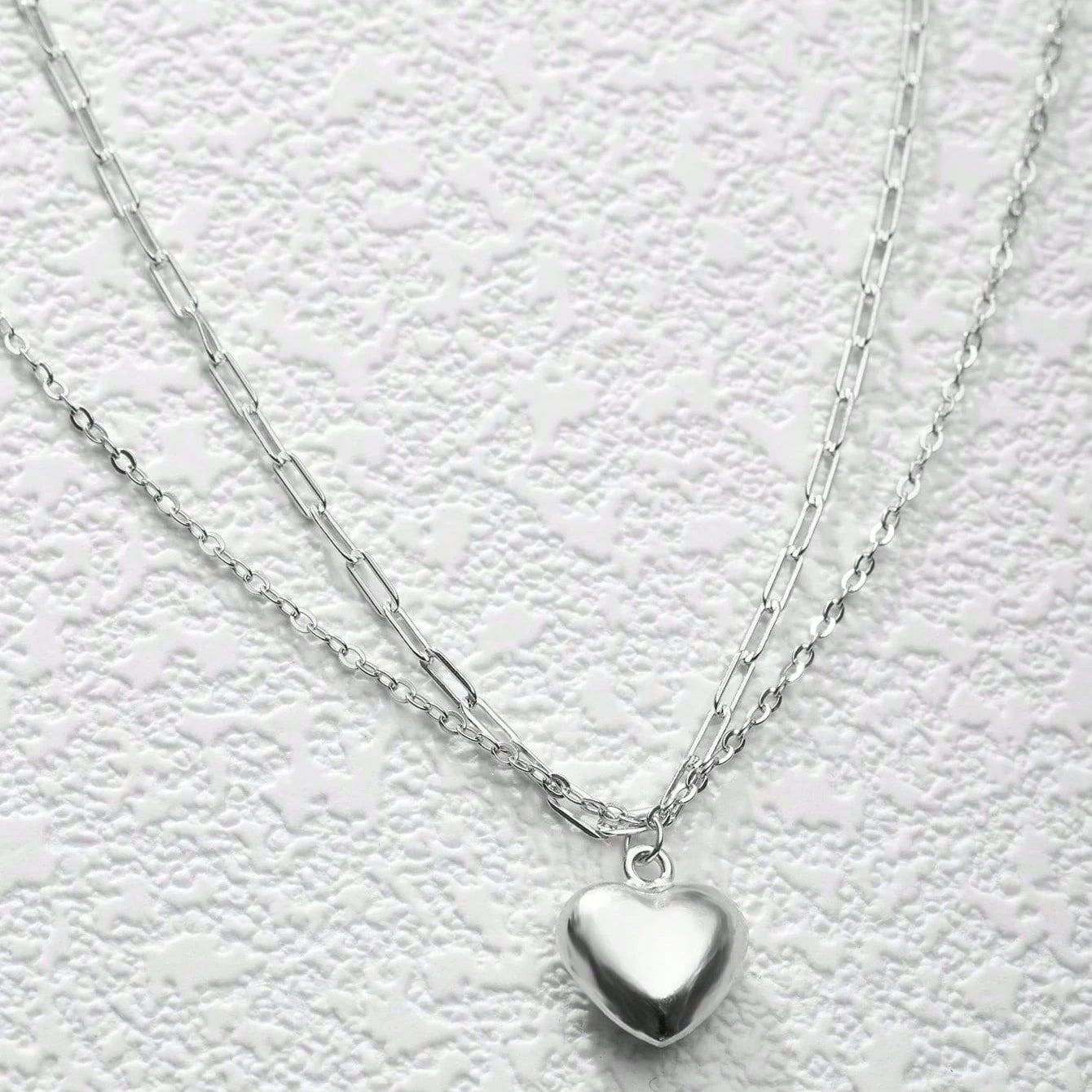 Silver heart-shaped pendant necklace on a textured white background