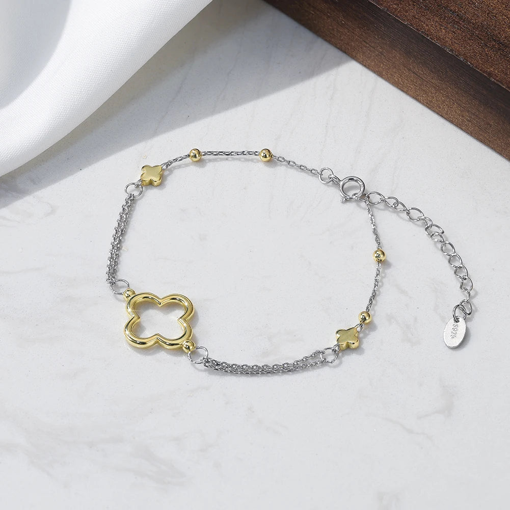 Silver and gold bracelet with clover-shaped charms on a white marble surface.