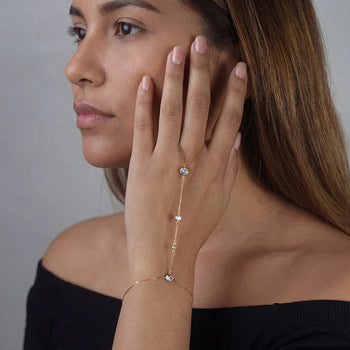 Woman wearing a delicate gold bracelet with small stones on a plain background