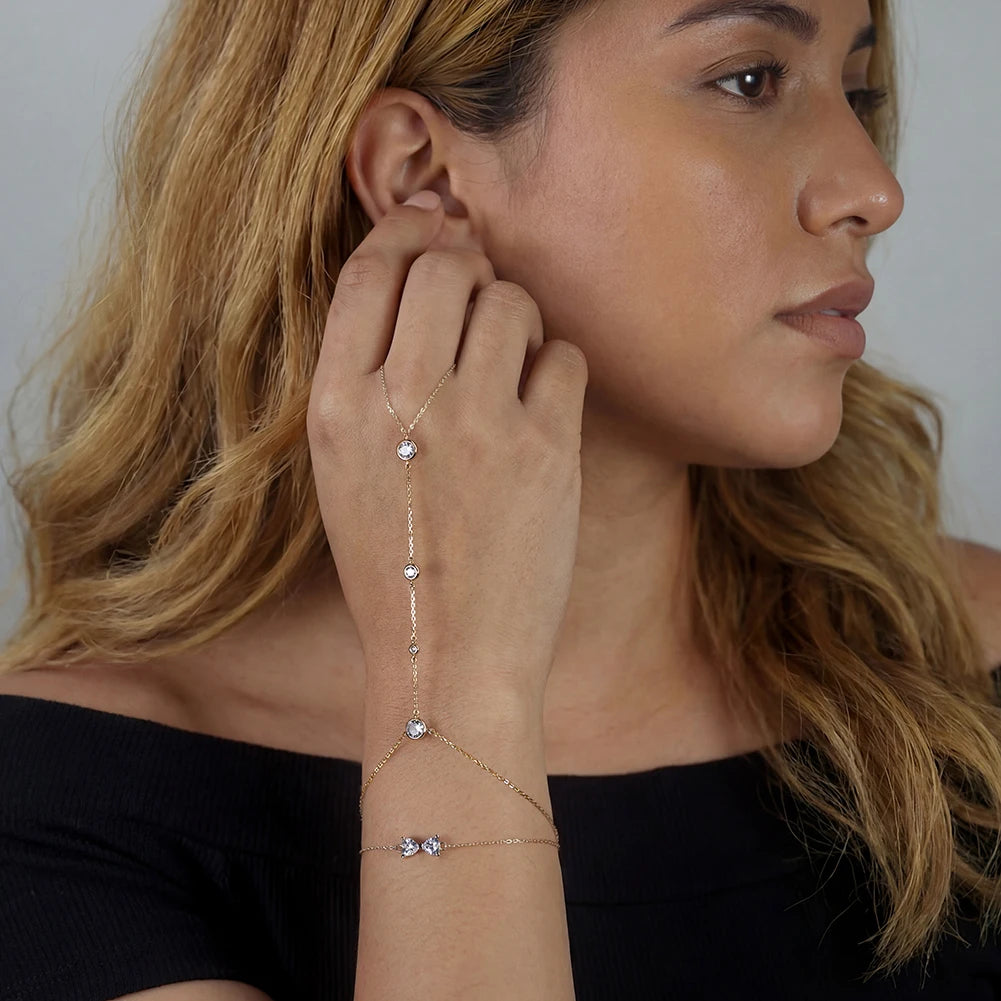 Woman wearing a delicate gold bracelet with small stones on a plain background