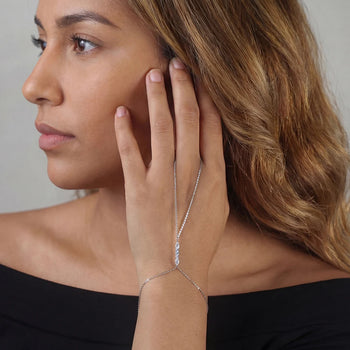 Woman wearing a delicate silver bracelet with a clear gemstone on a neutral background
