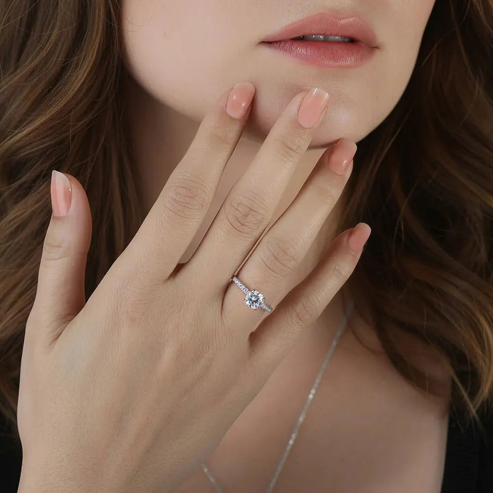 Close-up of a hand wearing a silver ring with a diamond, held near the face.
