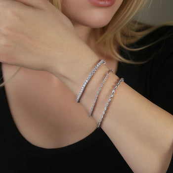 Close-up of a person's arm wearing three silver bracelets on a dark background