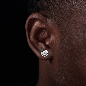 Close-up of an ear wearing a silver earring with a clear gemstone on a dark background