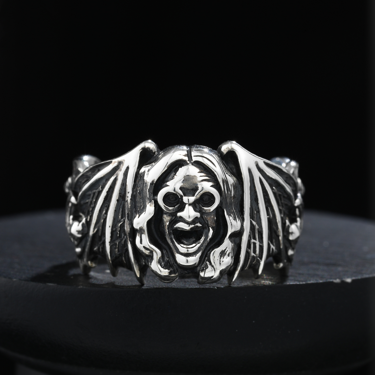 Silver bat-shaped ring with a face design on a black background