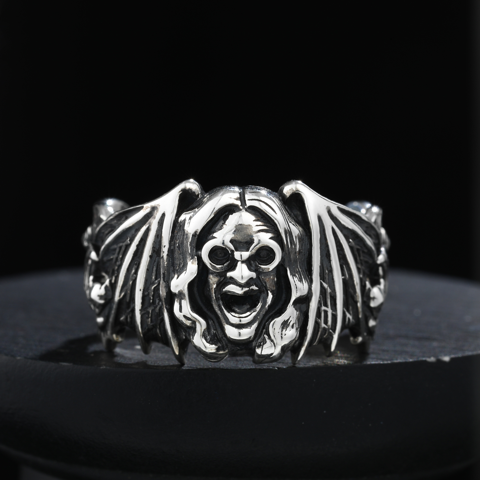 Silver bat-shaped ring with a face design on a black background