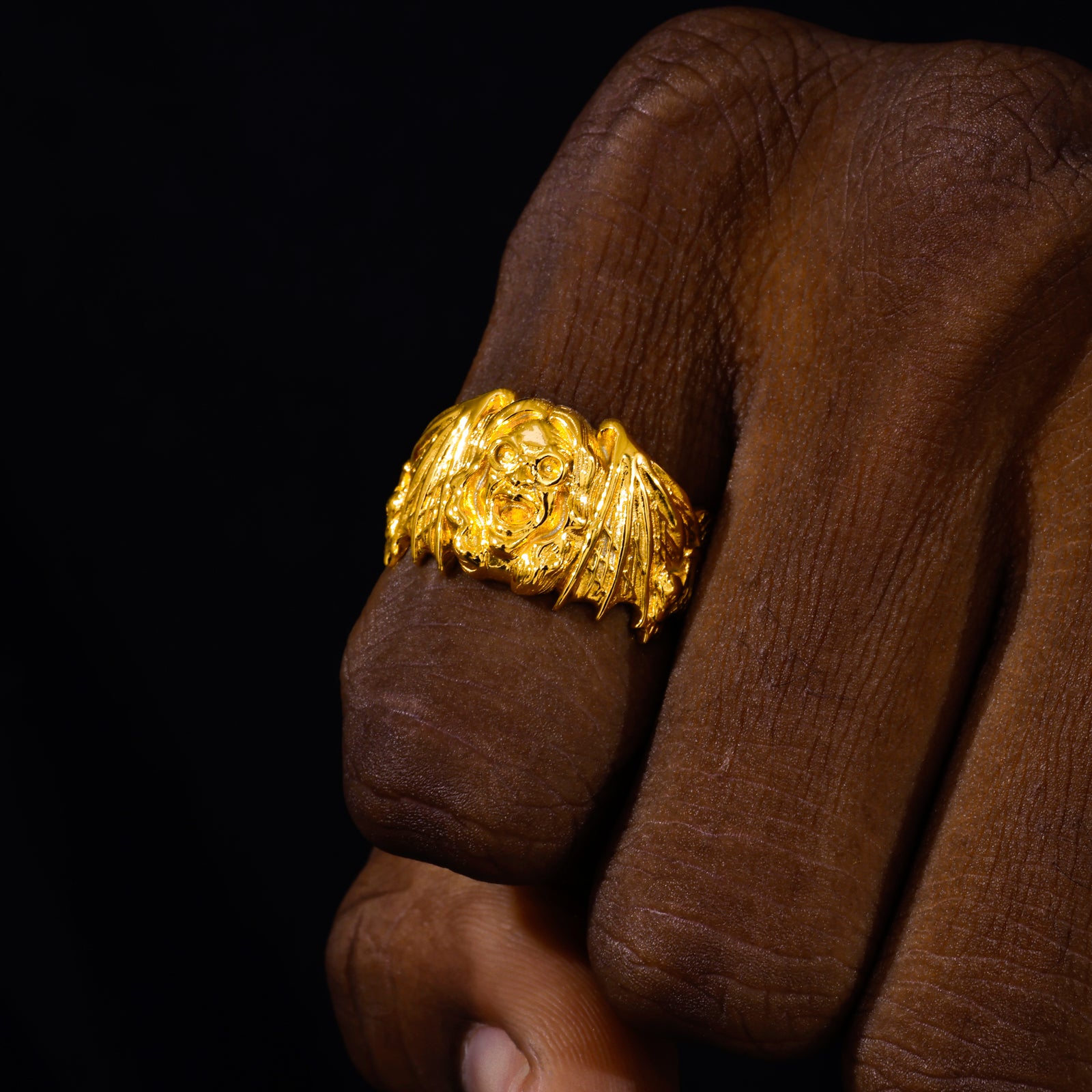 Gold ring with a detailed design on a brown hand against a black background