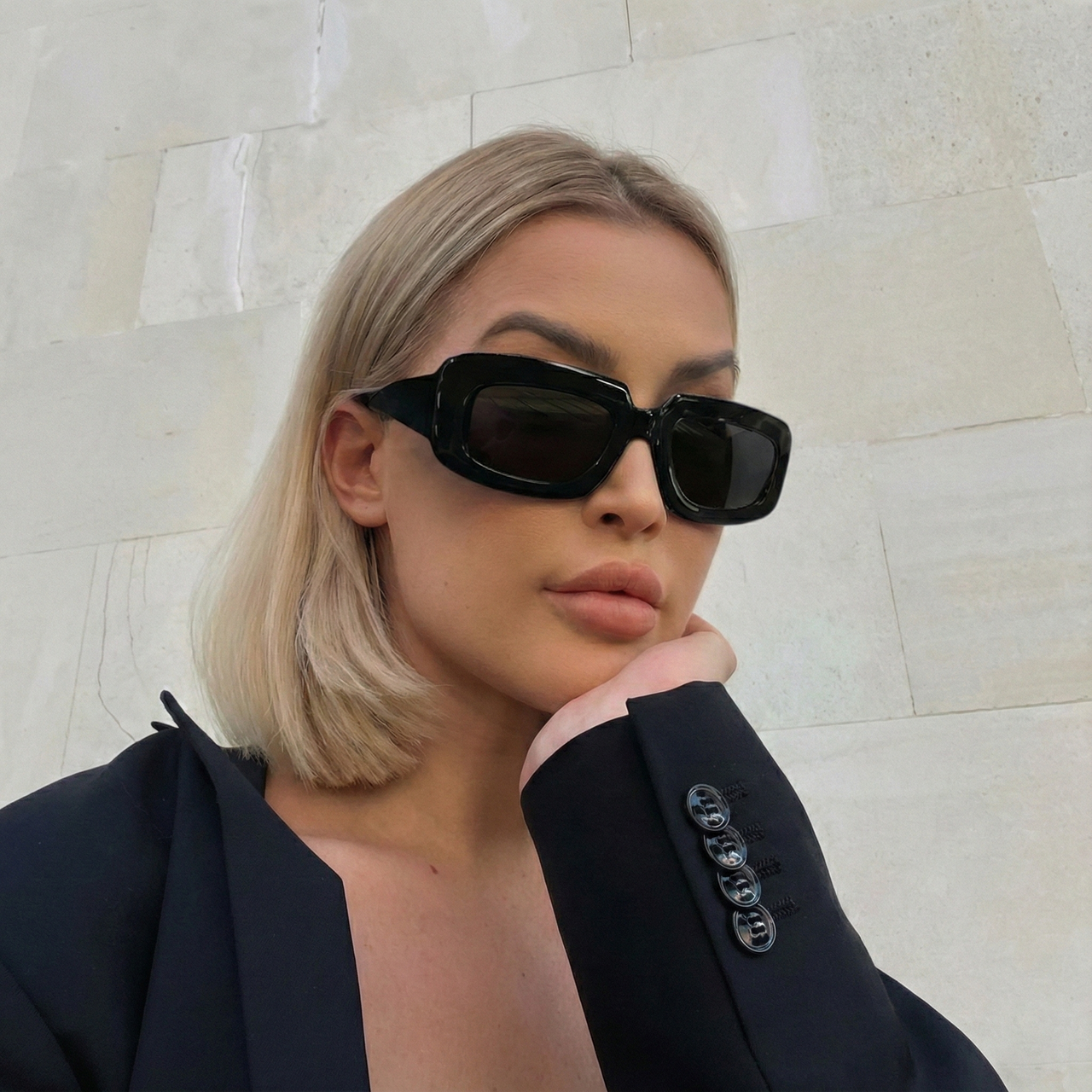 Man wearing black sunglasses and a dark coat against a neutral background