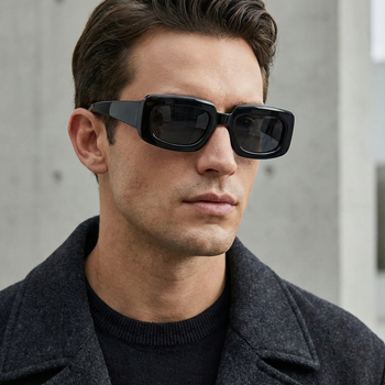 Man wearing black sunglasses and a dark coat against a neutral background